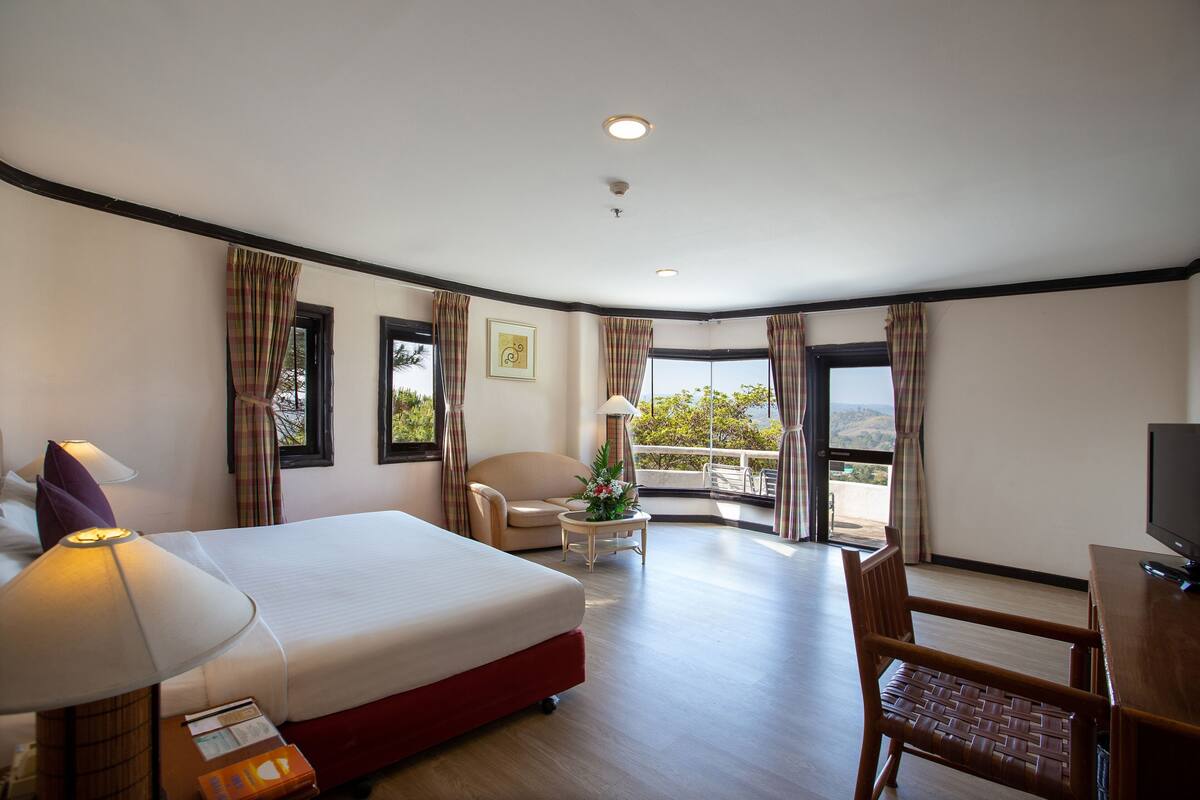 A hotel room with a bed, a desk, a chair, a lamp, and a view of the outdoors.