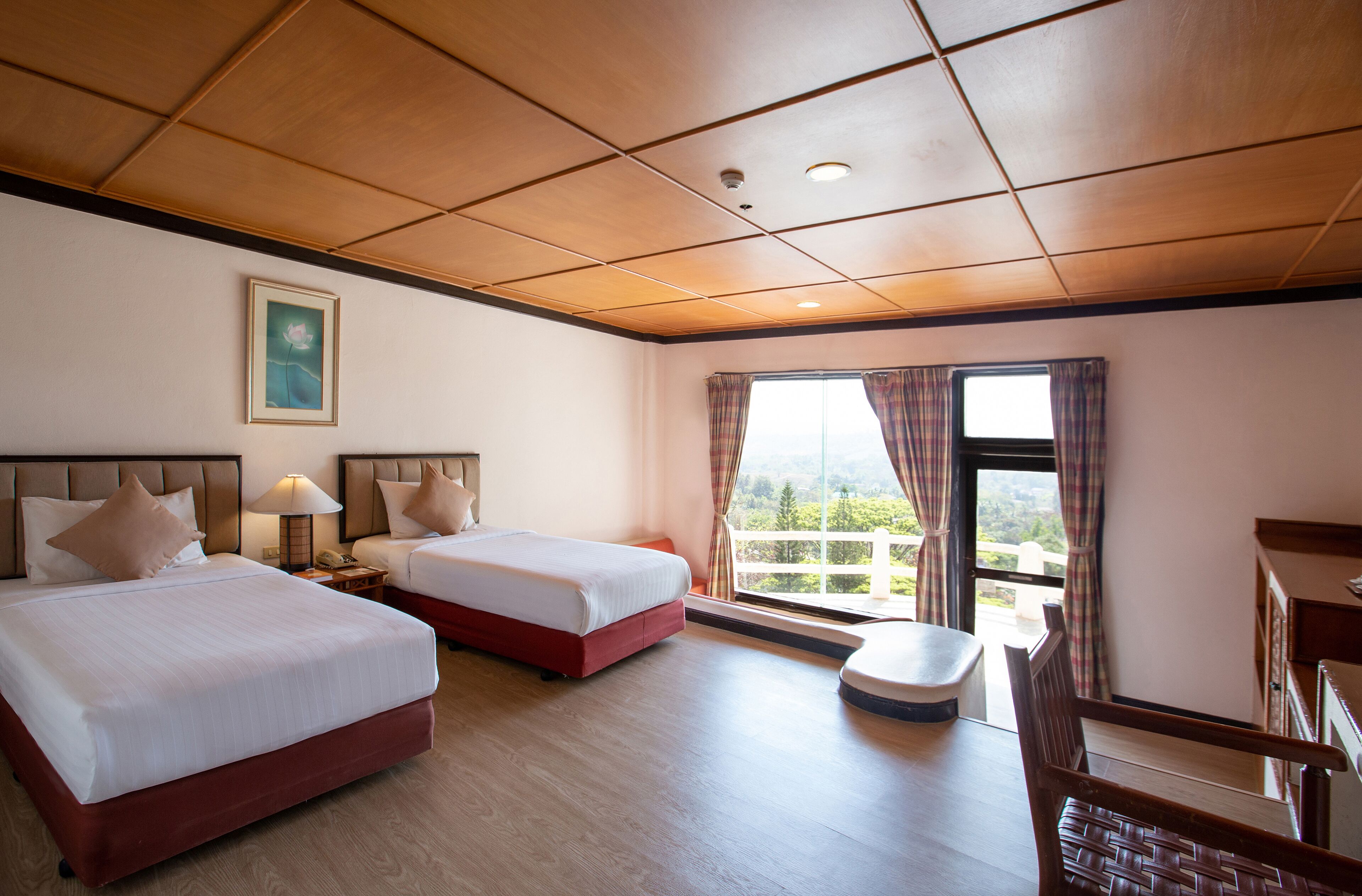 A hotel room with two beds, a desk, a chair, a window with curtains, and a painting on the wall.
