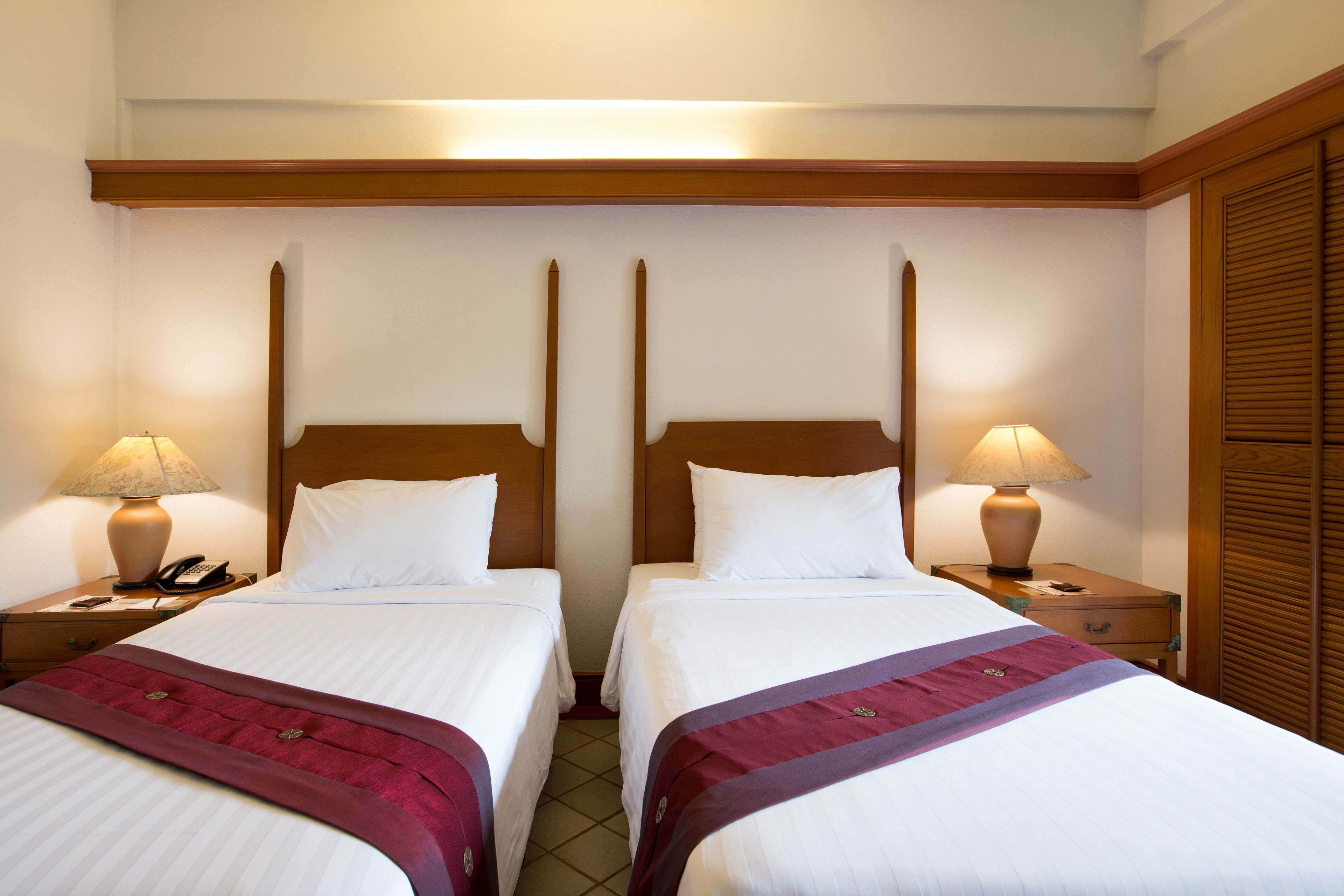 Habitación de hotel con dos camas individuales, cabeceros de madera, lámparas de noche, un teléfono y un armario de madera.