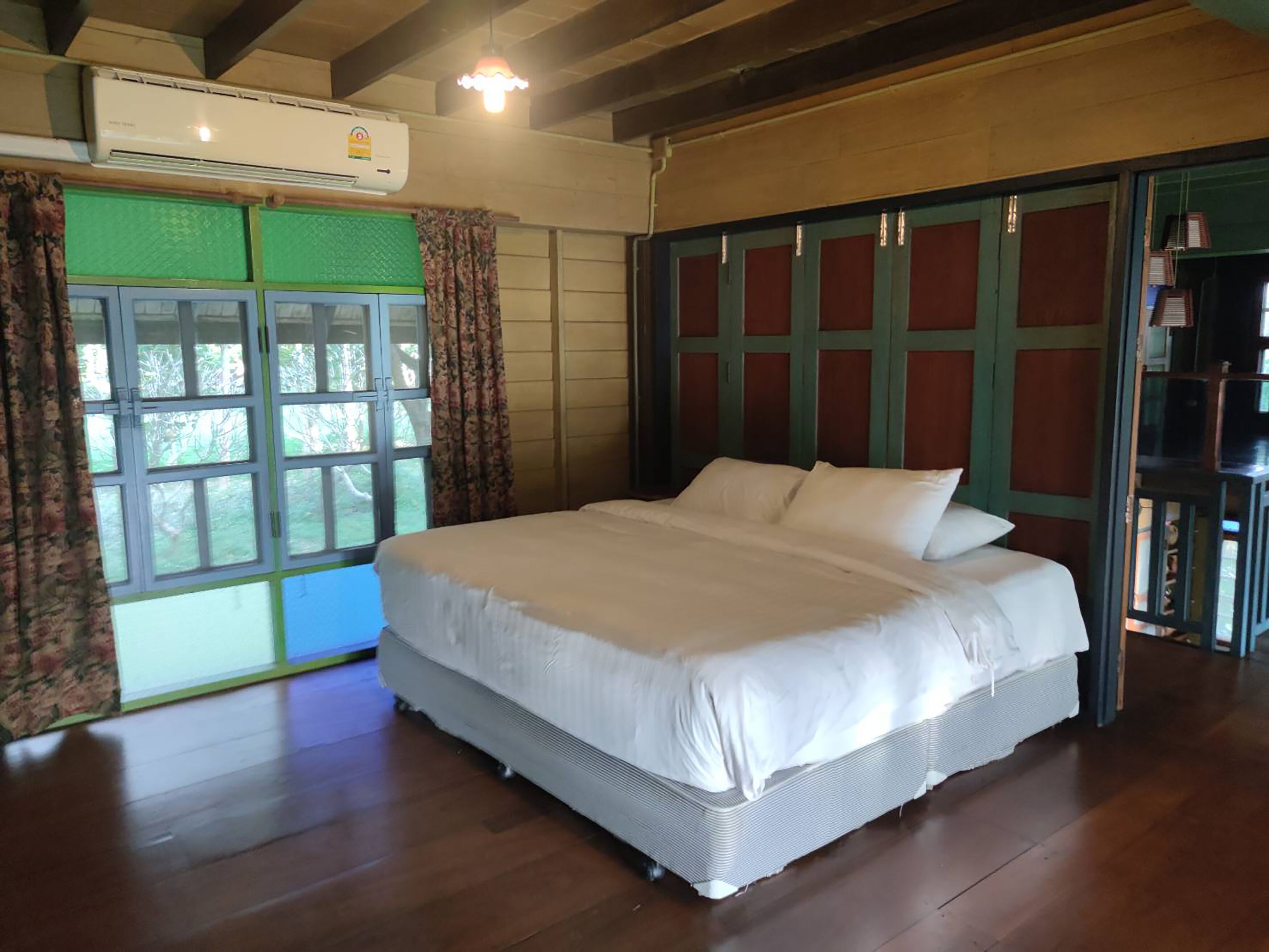 Un dormitorio con una cama grande, un equipo de aire acondicionado, una ventana con cortinas y piso de madera.
