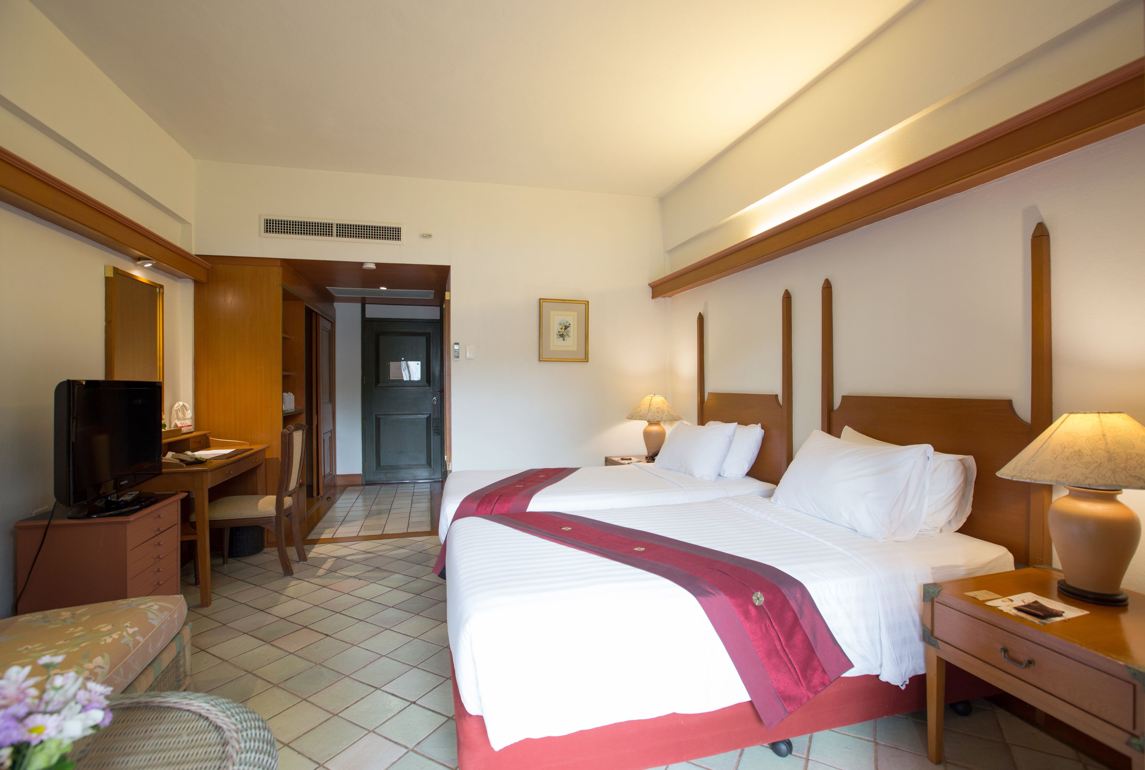 A hotel room with a large bed, a desk with a television, a chair, and a lamp.