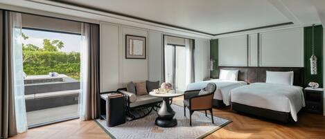 A hotel room with a large bed, a sofa, a dining table, and a view of greenery outside.