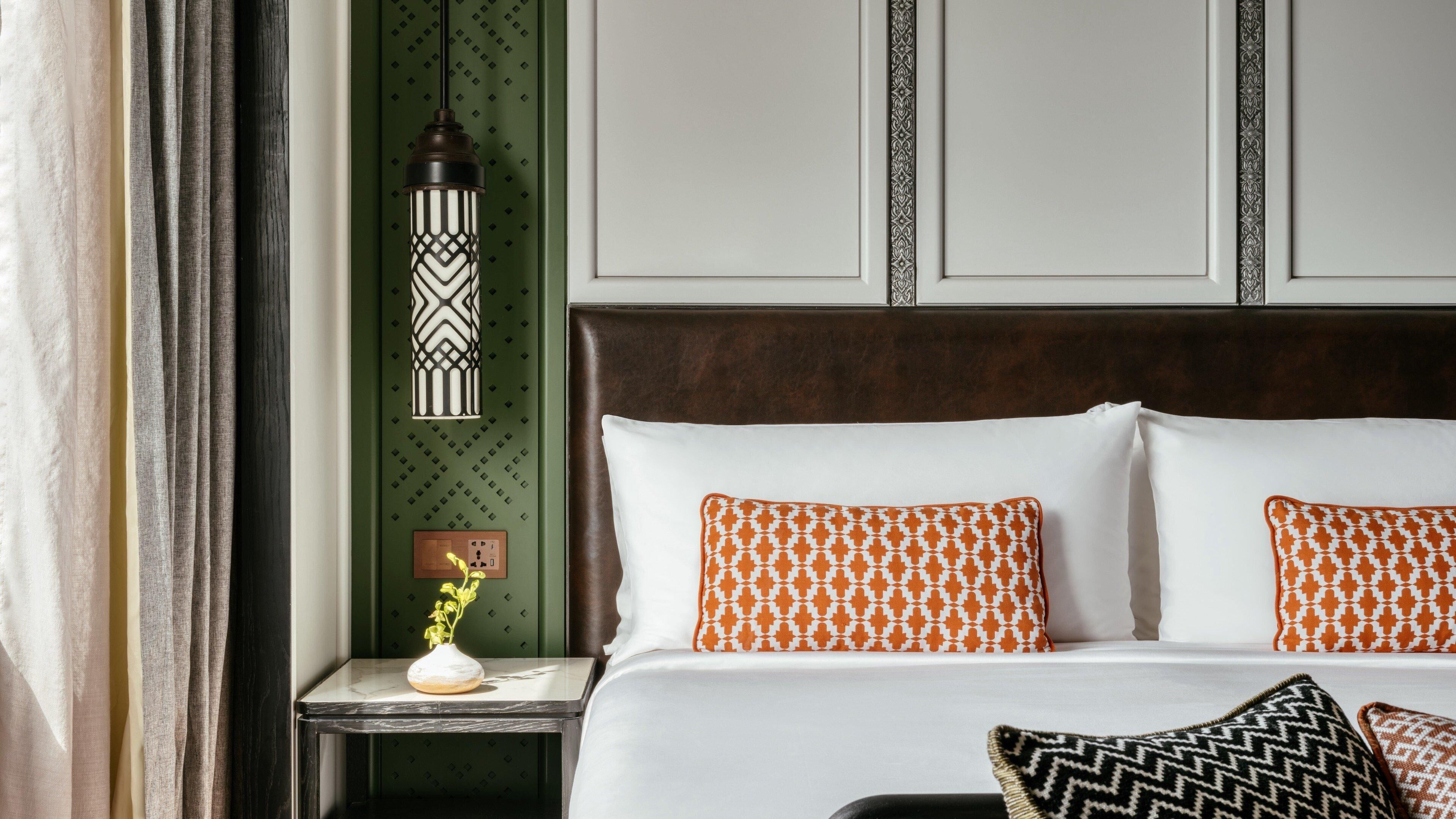 A hotel room with a bed, a nightstand with a vase, a wall-mounted lamp, and a decorative panel.