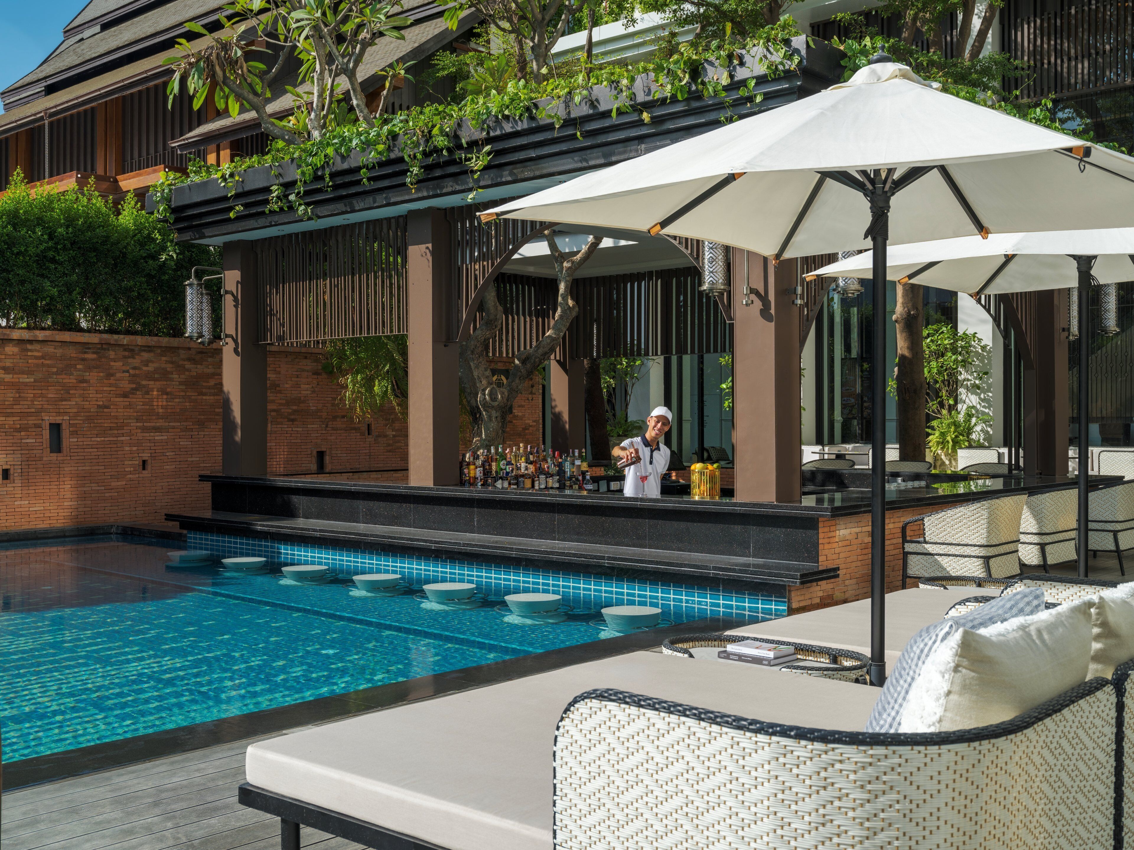 A poolside area with lounge chairs, a bartender, and a bar with a variety of bottles.