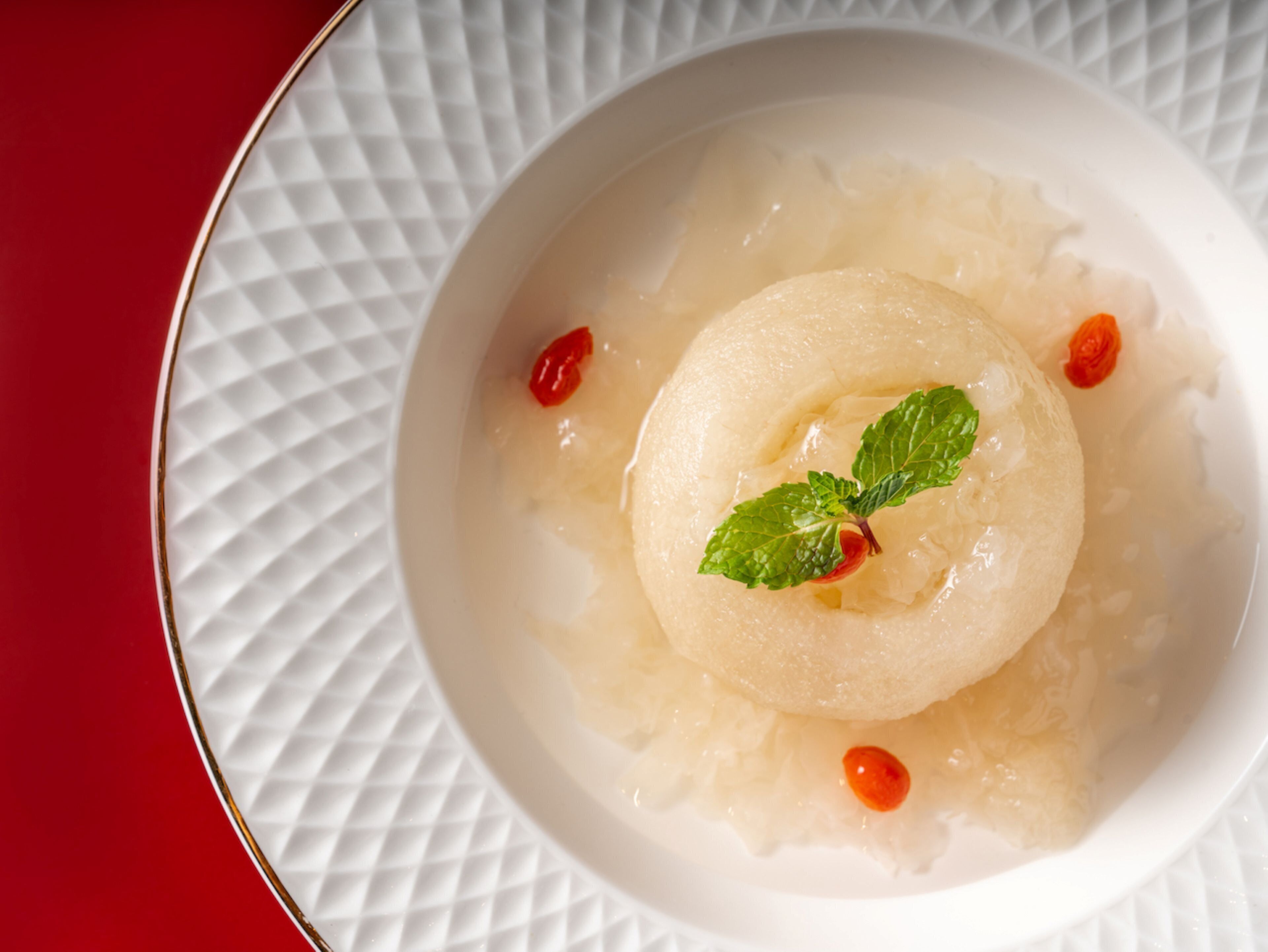 Un cuenco blanco con un postre sobre un plato blanco con textura.