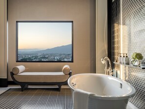 Une salle de bain moderne avec une grande baignoire, un banc agrémenté de coussins, une grande fenêtre donnant sur la ville et un mur décoratif orné de motifs géométriques.