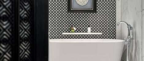 A modern bathroom with a freestanding bathtub, a framed decorative piece on the wall, and a shower area.