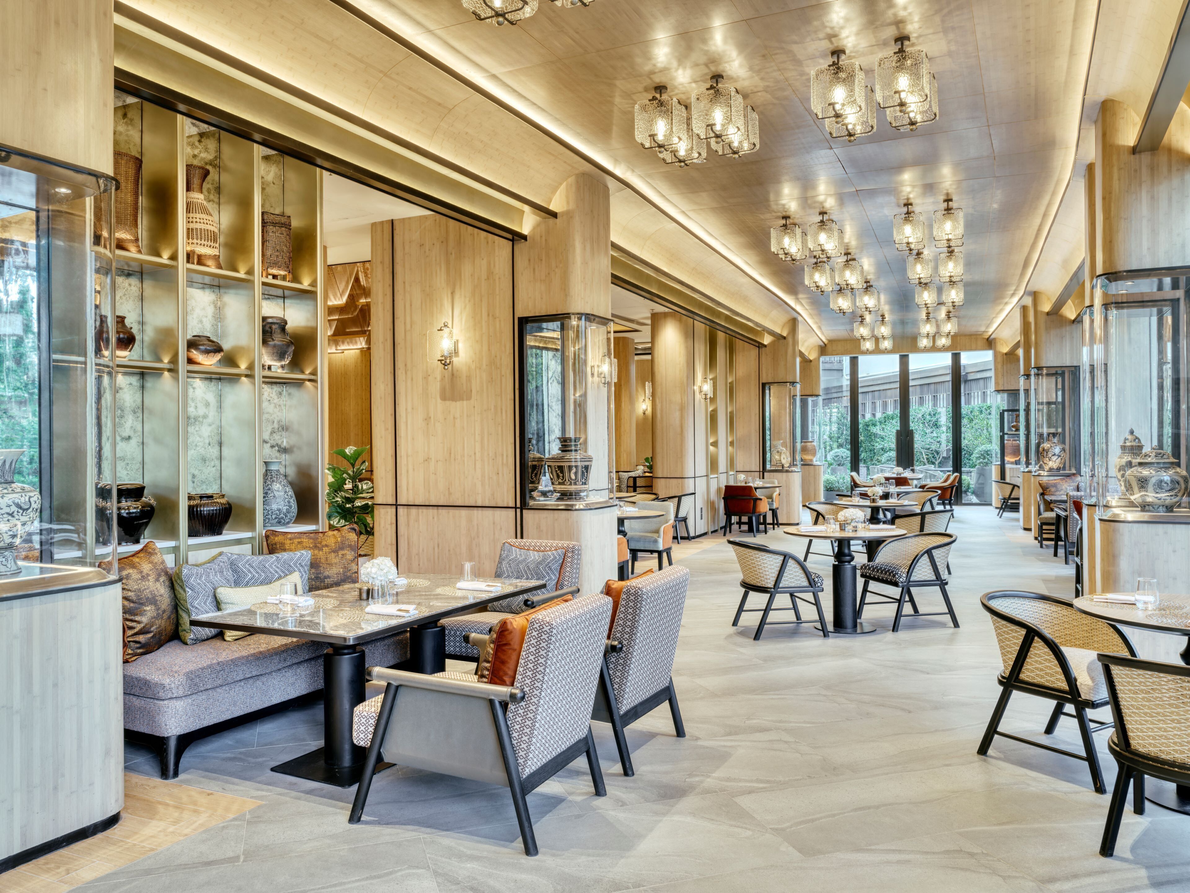 A spacious restaurant with high ceilings, modern chandeliers, and a variety of seating arrangements including tables and booths.