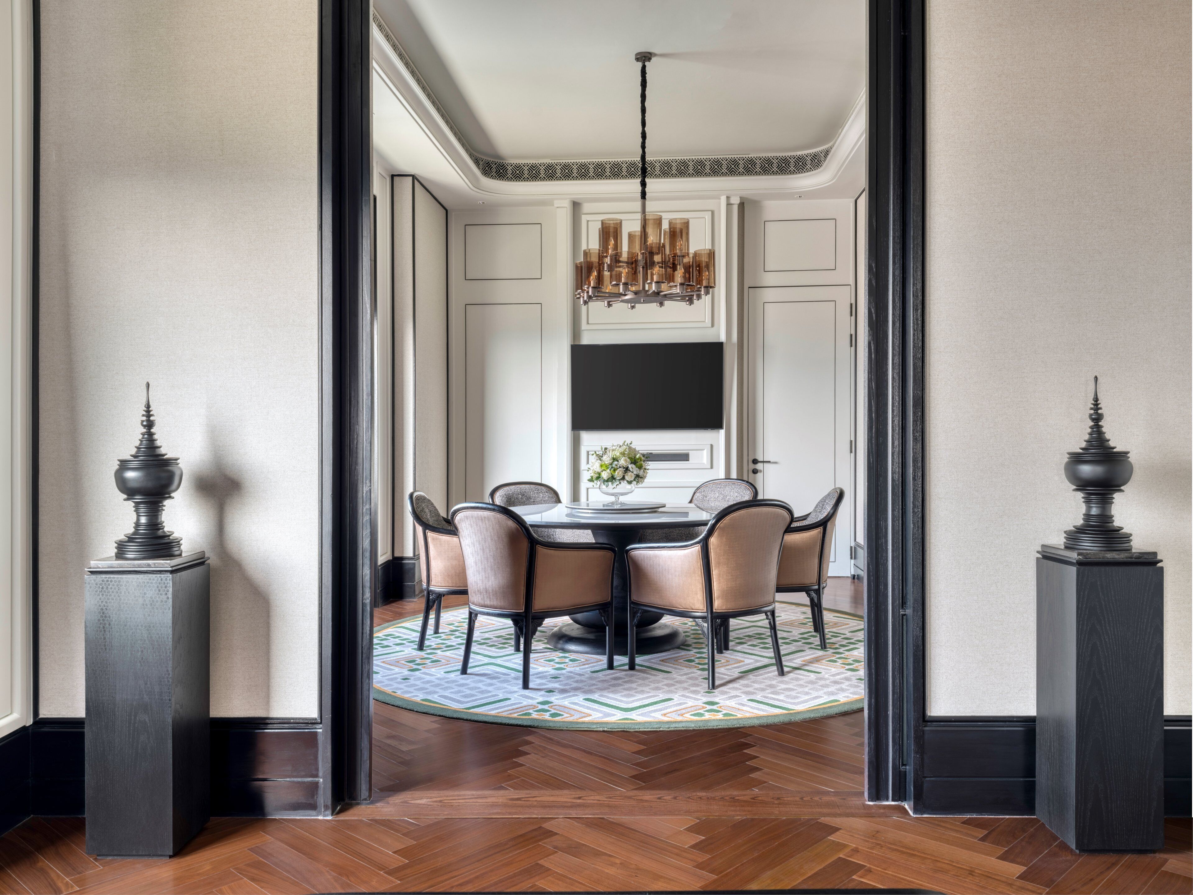 Un comedor con una mesa redonda, seis sillas, una araña y jarrones decorativos.