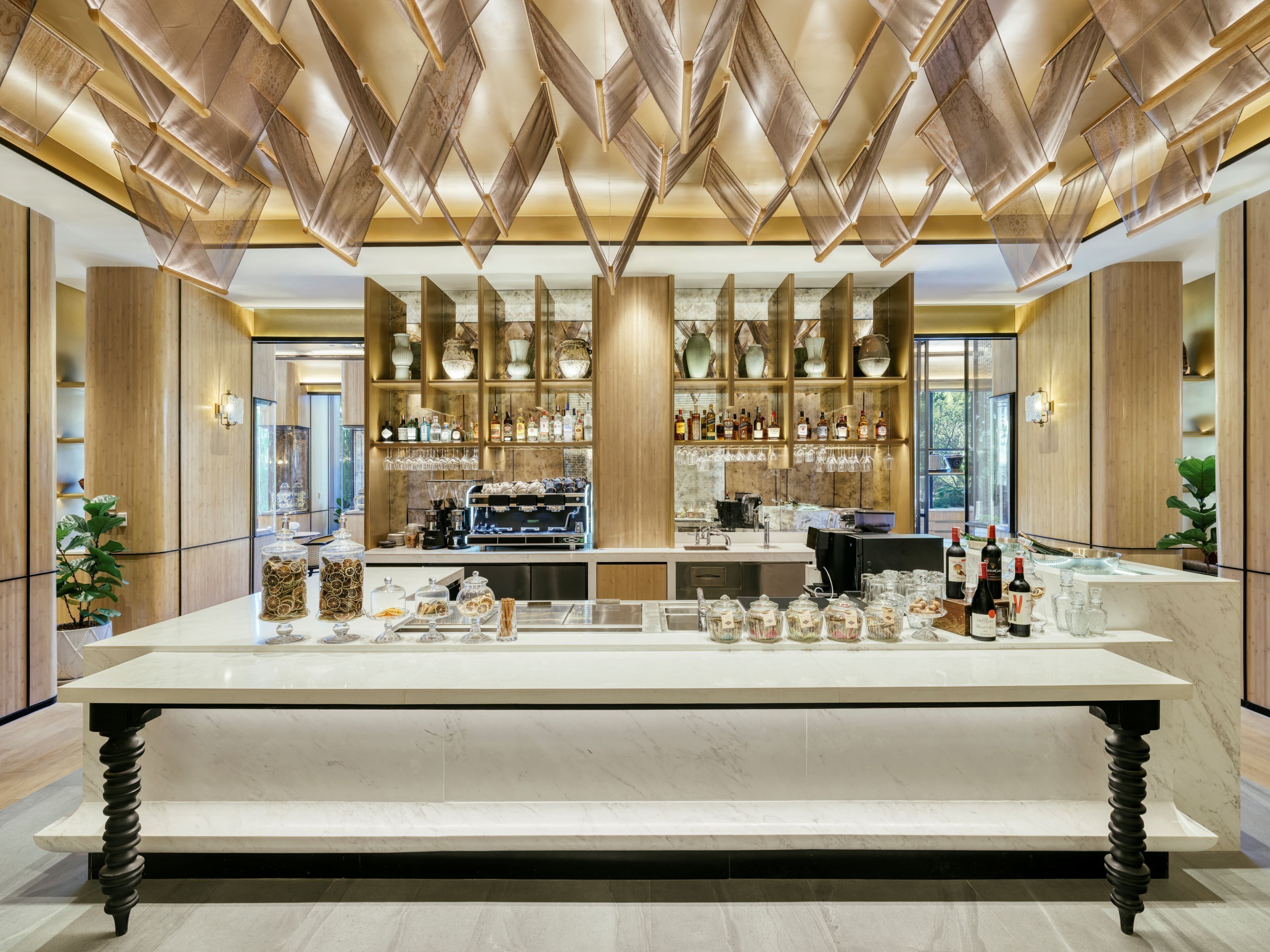 A modern bar area with a marble countertop, a coffee machine, and shelves stocked with bottles and glasses.