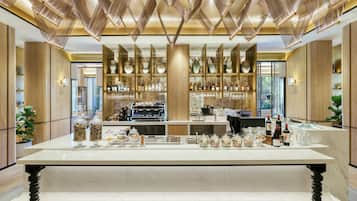 A modern bar area with a marble countertop, a coffee machine, and shelves stocked with bottles and glasses.