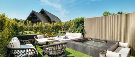 A modern outdoor patio with a hot tub, wicker furniture, and a wooden deck.