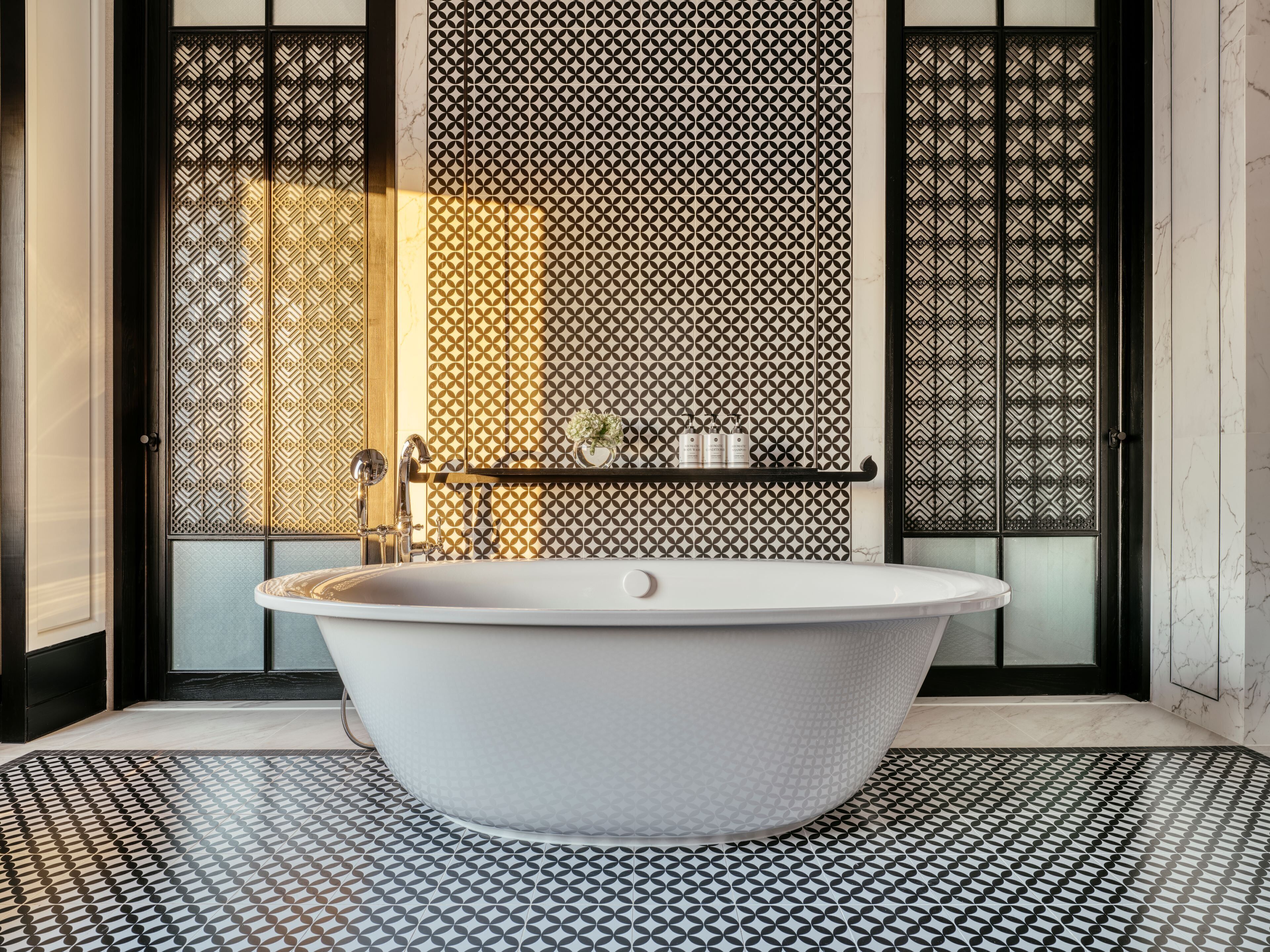 A modern bathroom with a freestanding bathtub, patterned floor tiles, and decorative screens.