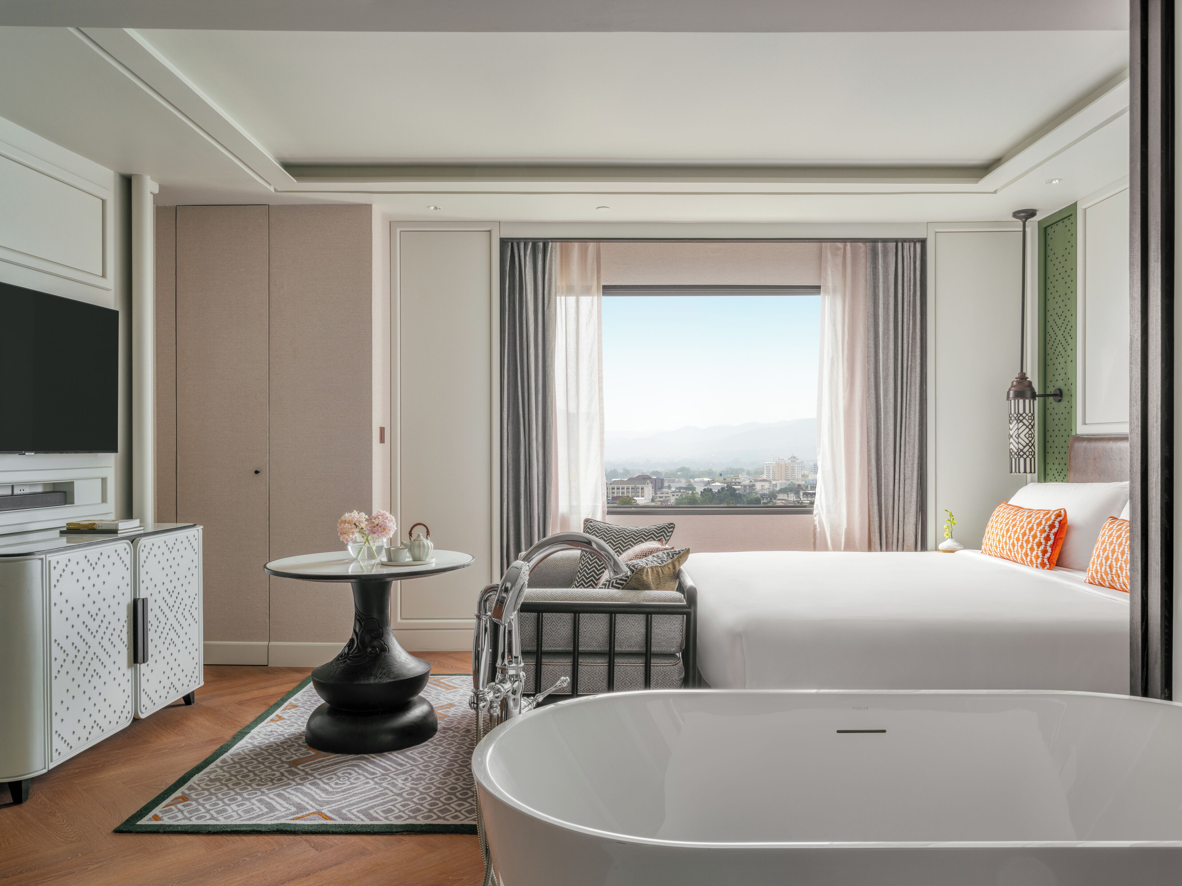 A modern hotel room with a large bed, a bathtub, a television, a desk, and a view of the city.