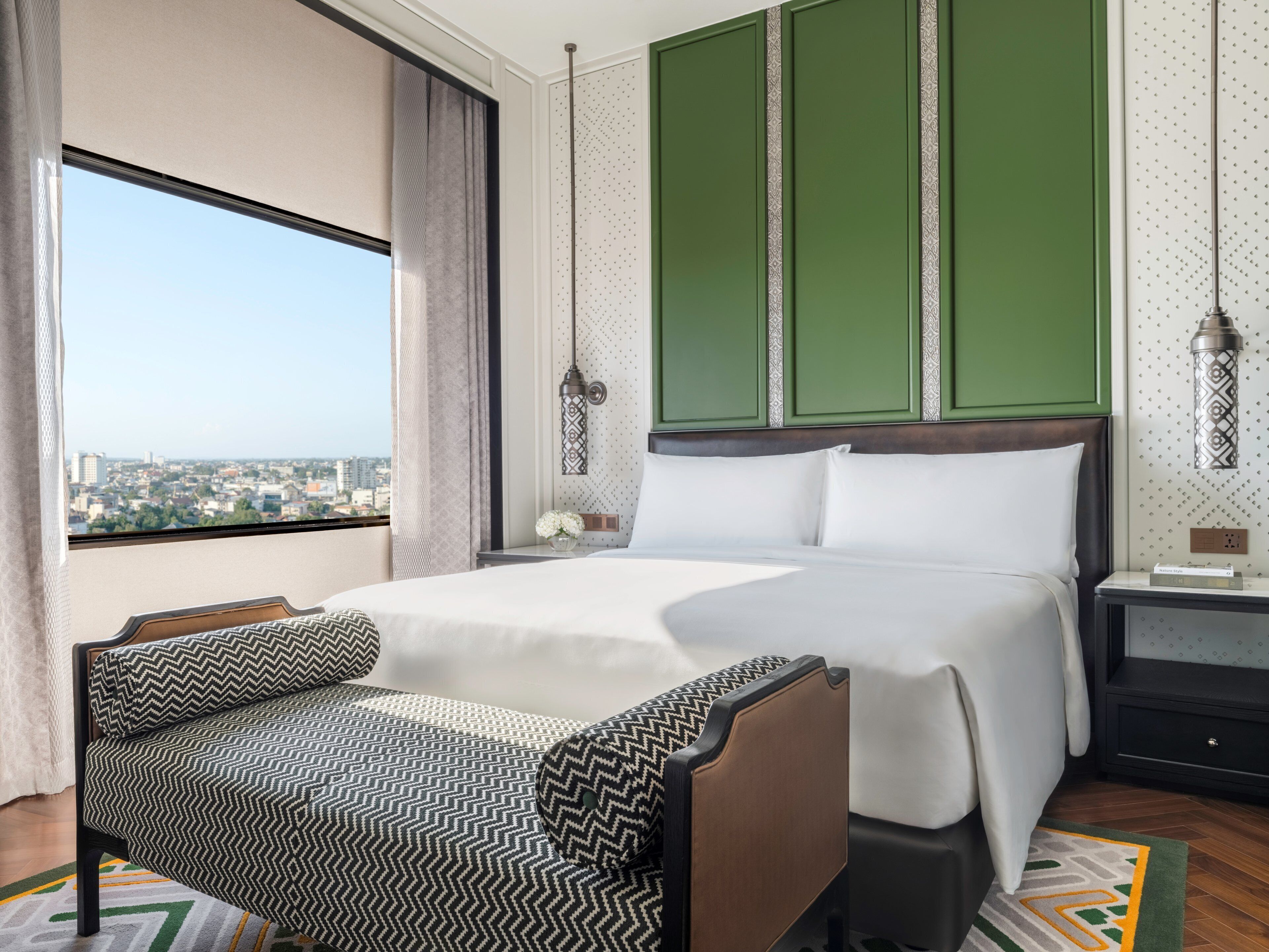 Habitación de hotel con una cama grande, una silla, una mesita de noche y vistas a la ciudad.