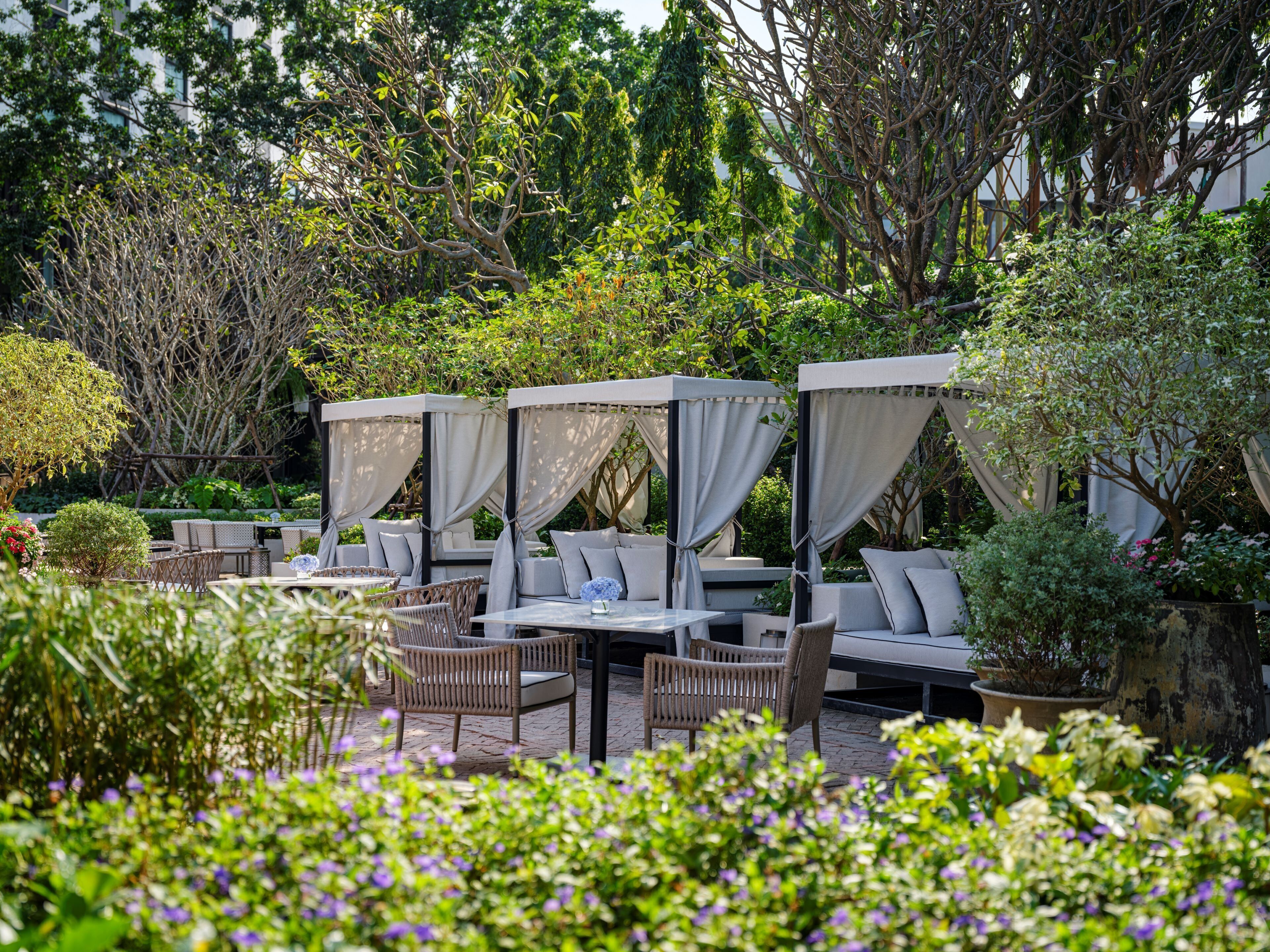 An outdoor seating area with cushioned chairs and tables, surrounded by lush greenery and trees.