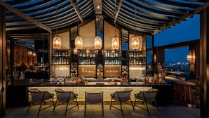 Zona de bar con diseño moderno, que incluye una barra con taburetes, lámparas colgantes y vistas nocturnas de la ciudad.