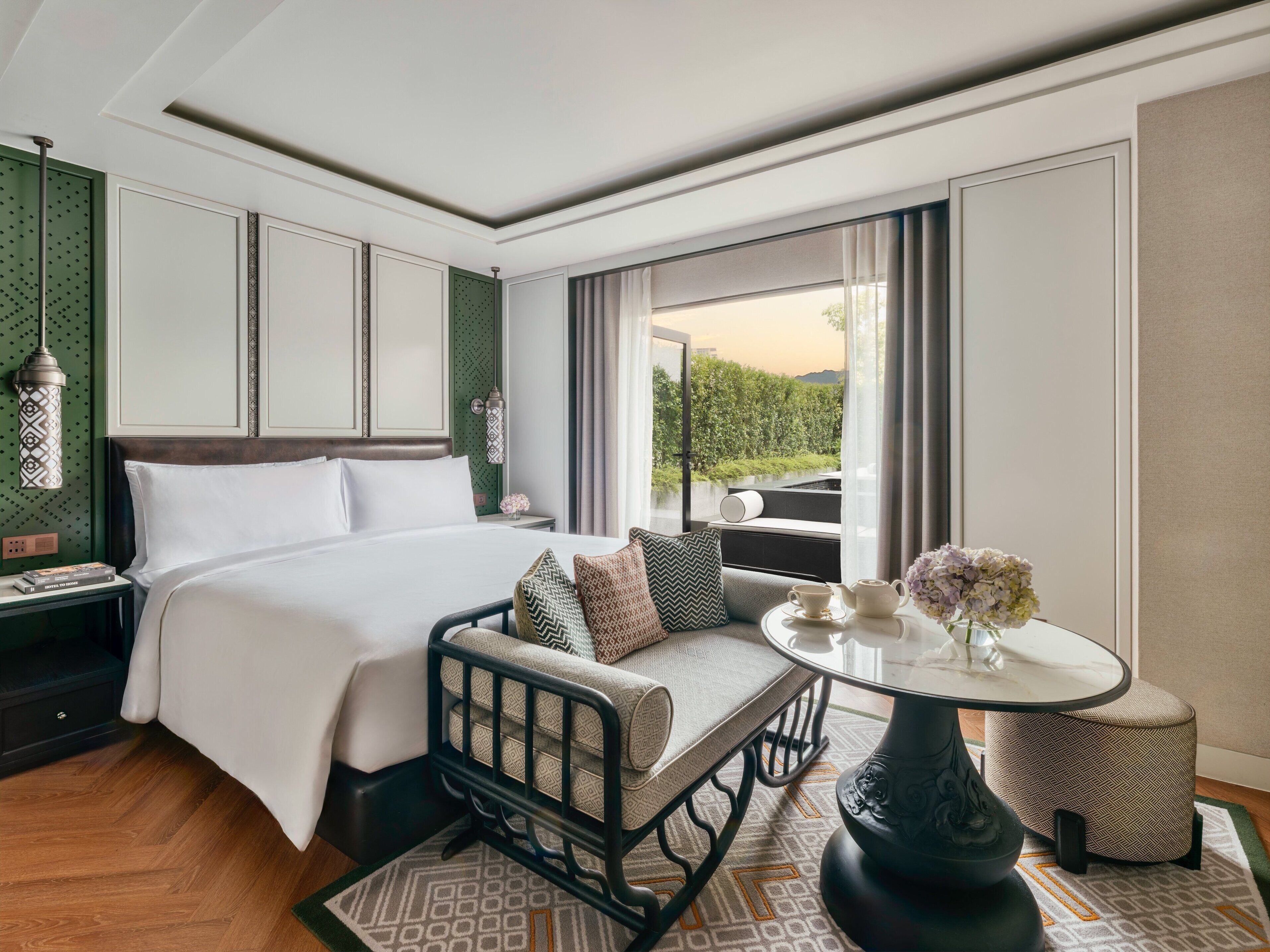 Habitación de hotel con una cama grande, zona de estar con una mesa y vistas a zonas verdes.