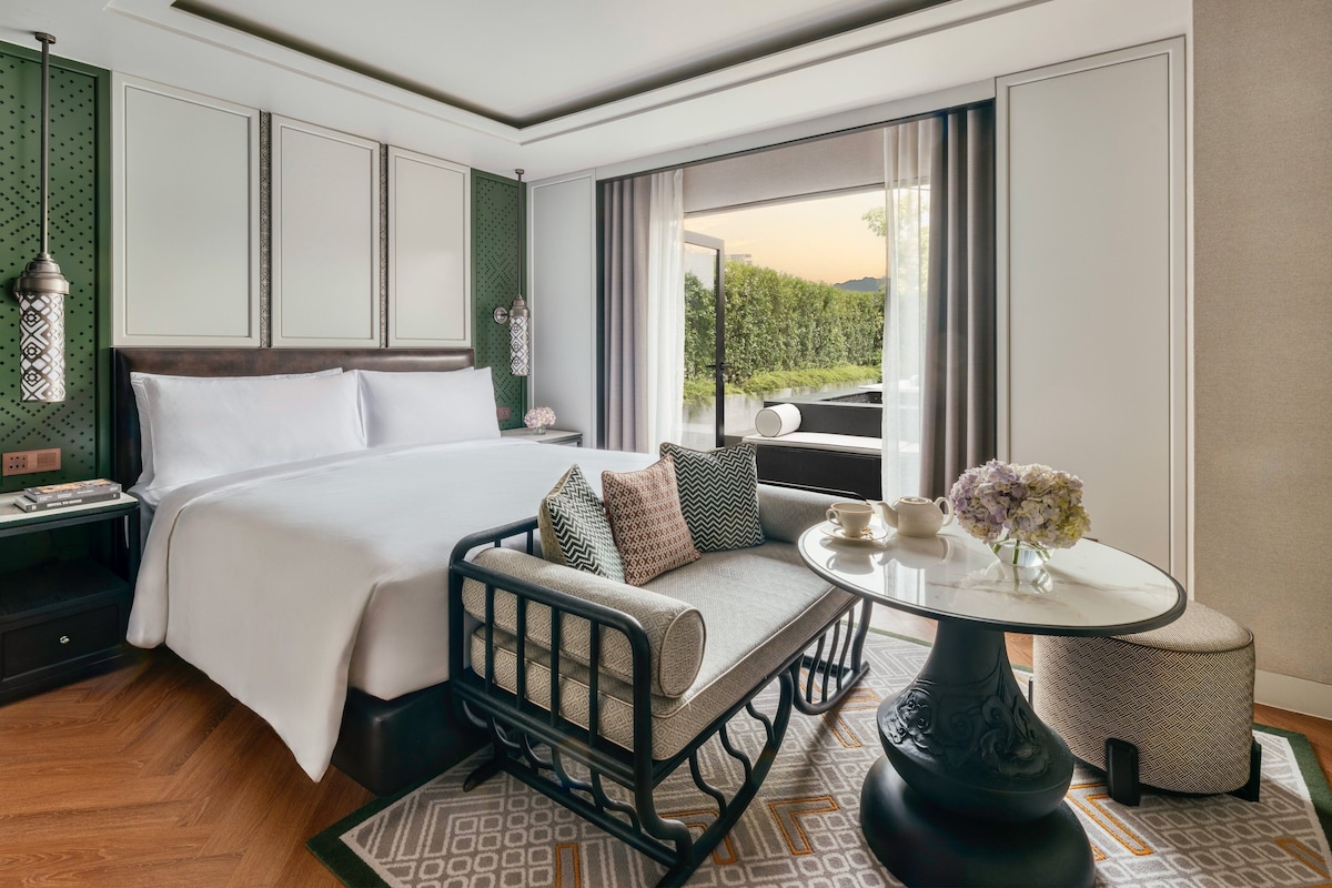 Ein Hotelzimmer mit einem großen Bett, einer Sitzecke mit Tisch und Blick auf Grünflächen.