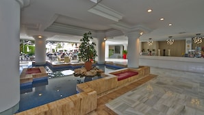 A spacious lobby with a central pool, seating areas, and a reception desk. - Illot Suites (Capdepera)