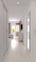 Un pasillo moderno de hotel con suelo plano, un espejo grande en un lateral, un televisor montado en la pared y una ventana con cortinas.