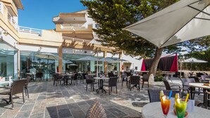 An outdoor patio area with stone flooring, wicker chairs, and tables with umbrellas. - Illot Suites (Capdepera)