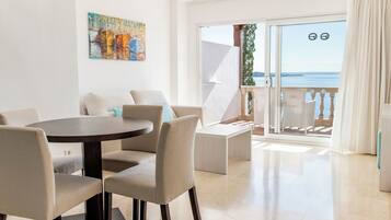 A modern living room with a round table and chairs, a painting on the wall, and a balcony with a view of the sea.