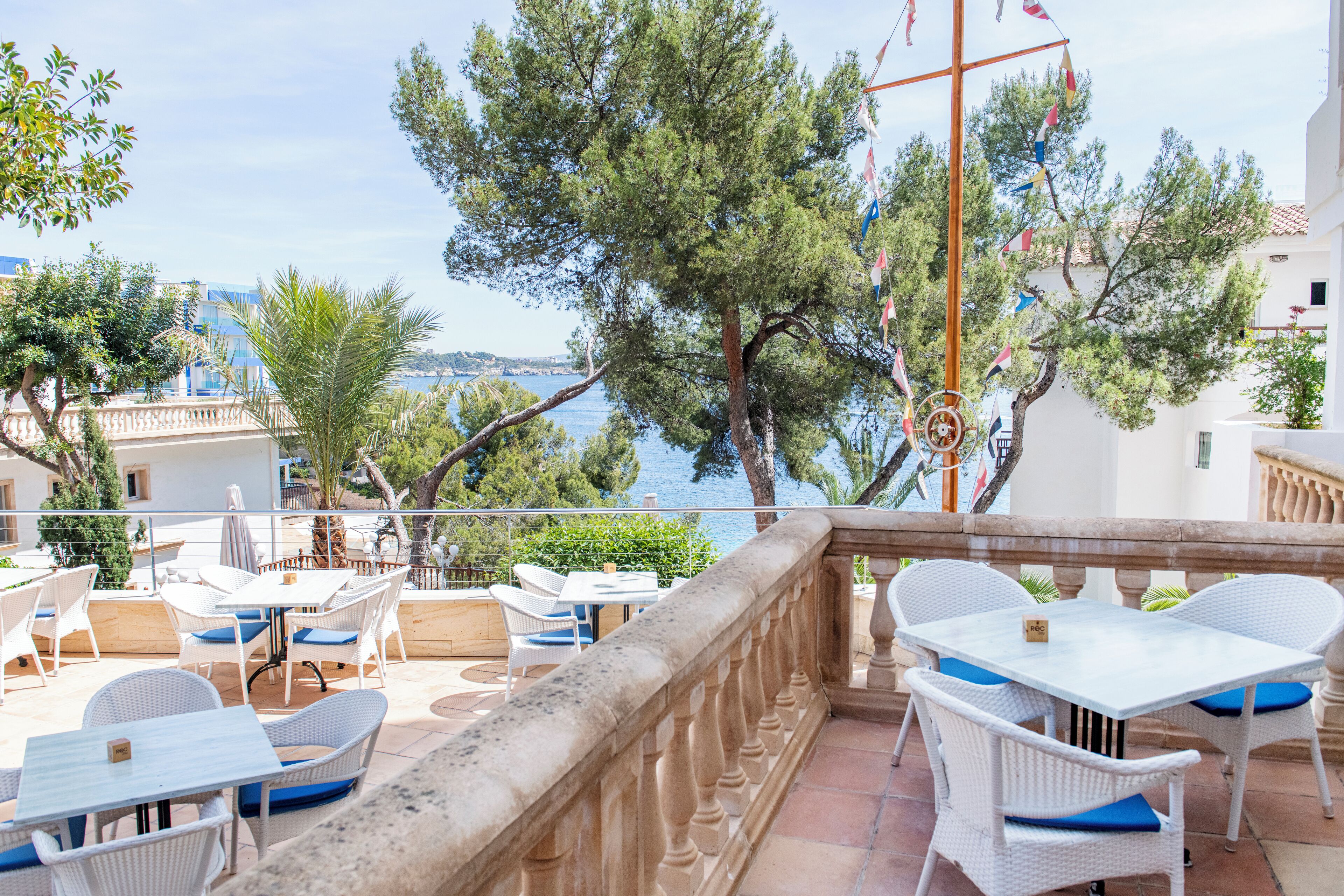 An outdoor terrace with white wicker furniture and a view of the sea.