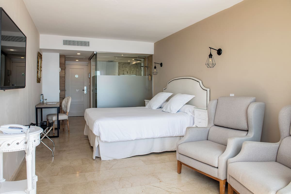 A hotel room with a bed, two armchairs, a desk, and a mirror.