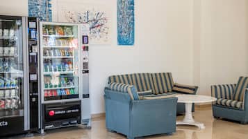 A vending machine with a variety of drinks and snacks, a blue striped sofa, and a small white table in a clean, modern lobby area.