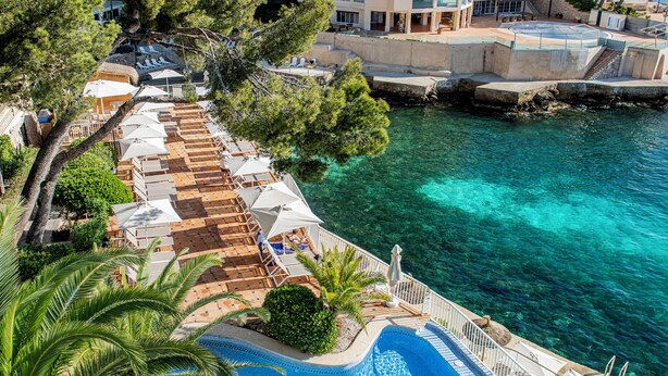 Piscina infinita con vista al mar, sillas de descanso y sombrillas.
