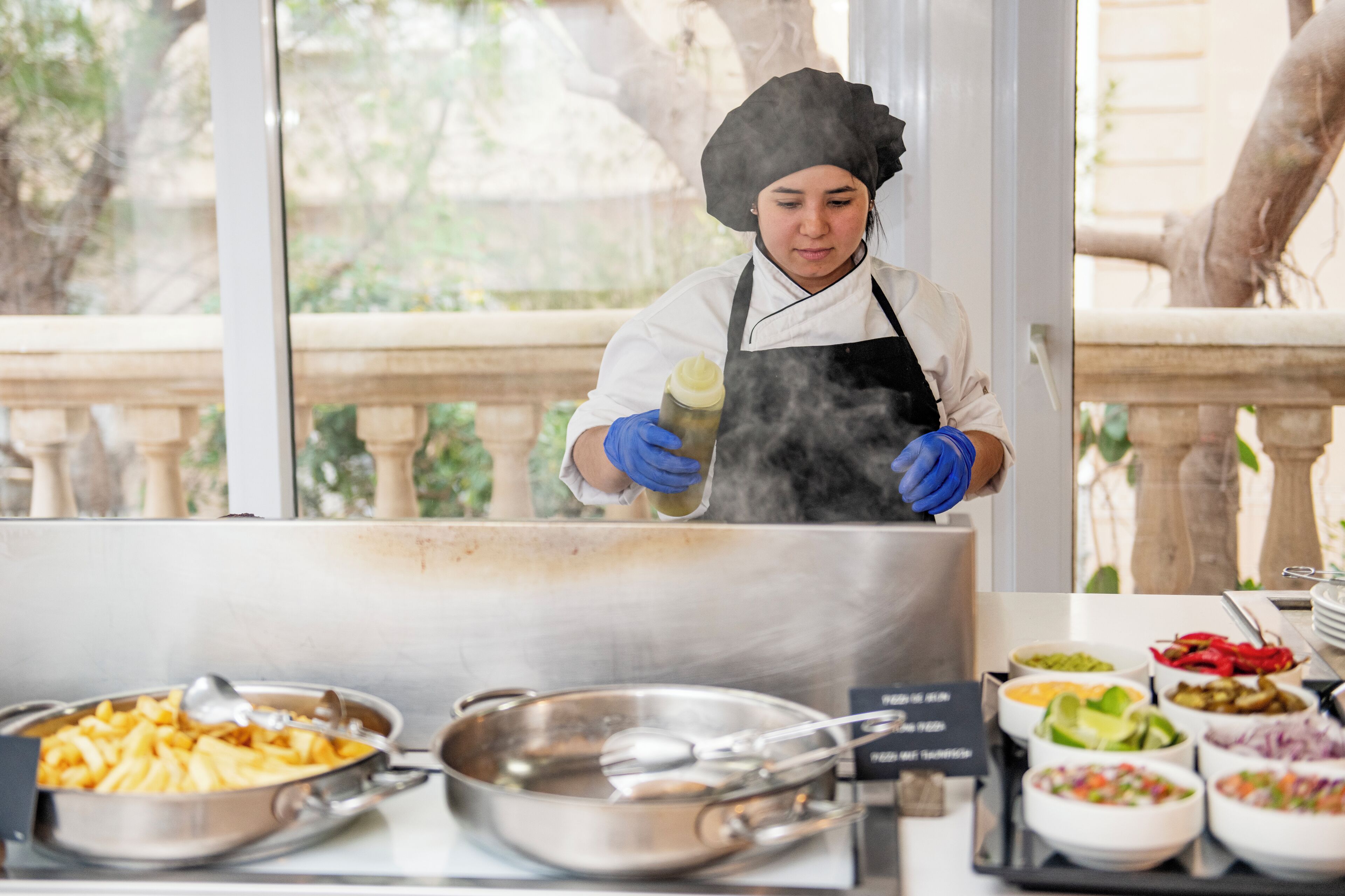 A chef preparing food in a kitchen with various dishes and cooking utensils visible.