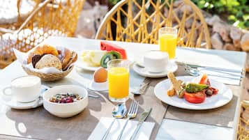 Ein Frühstückstisch mit Weidenstuhl, Teller mit Speisen, einem Brotkorb, einem Glas Orangensaft und einer Tasse Kaffee.