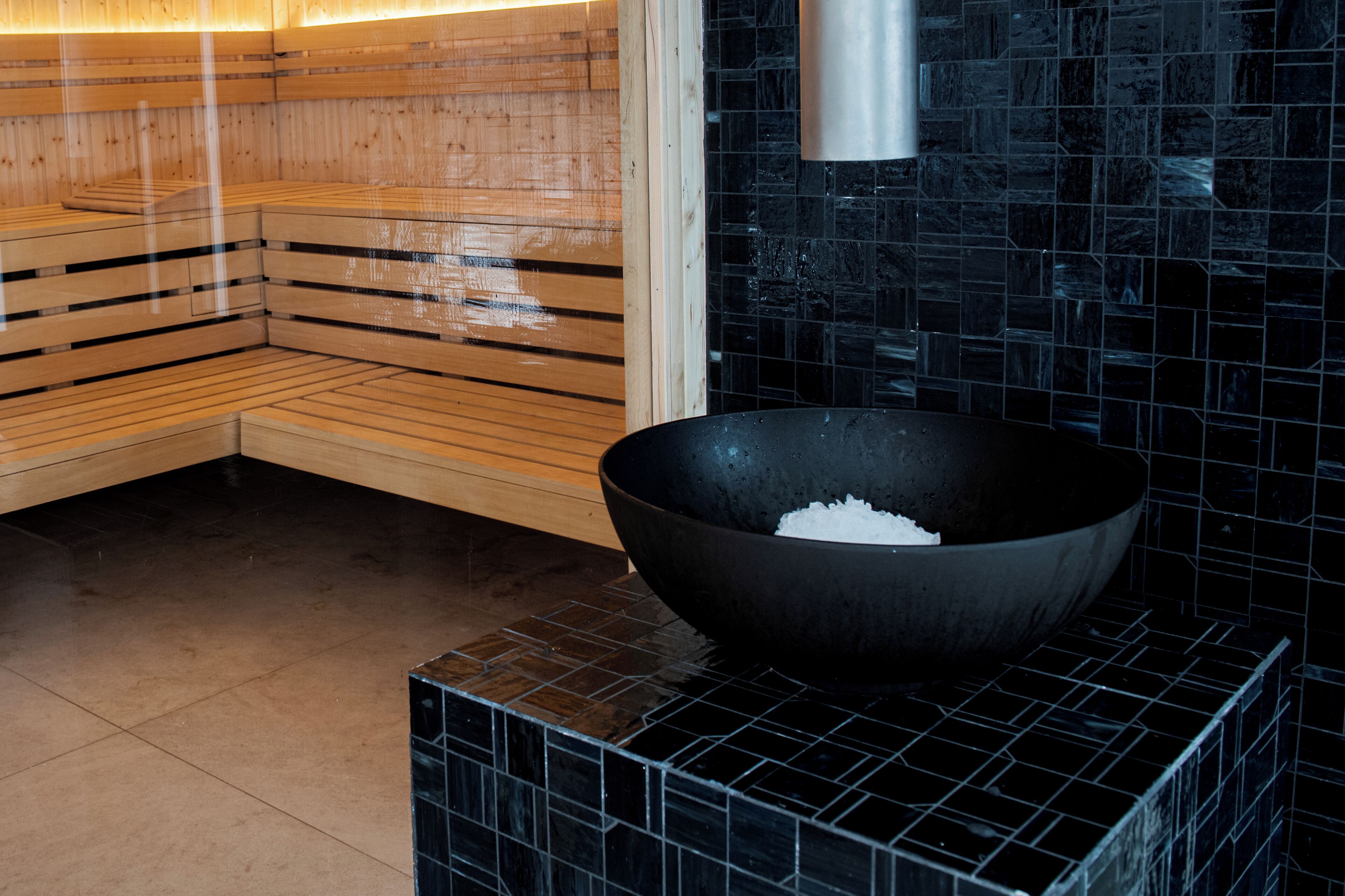 Una sauna con bancos de madera y pared de azulejos negros.