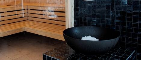 Una sauna con bancos de madera y pared de azulejos negros.