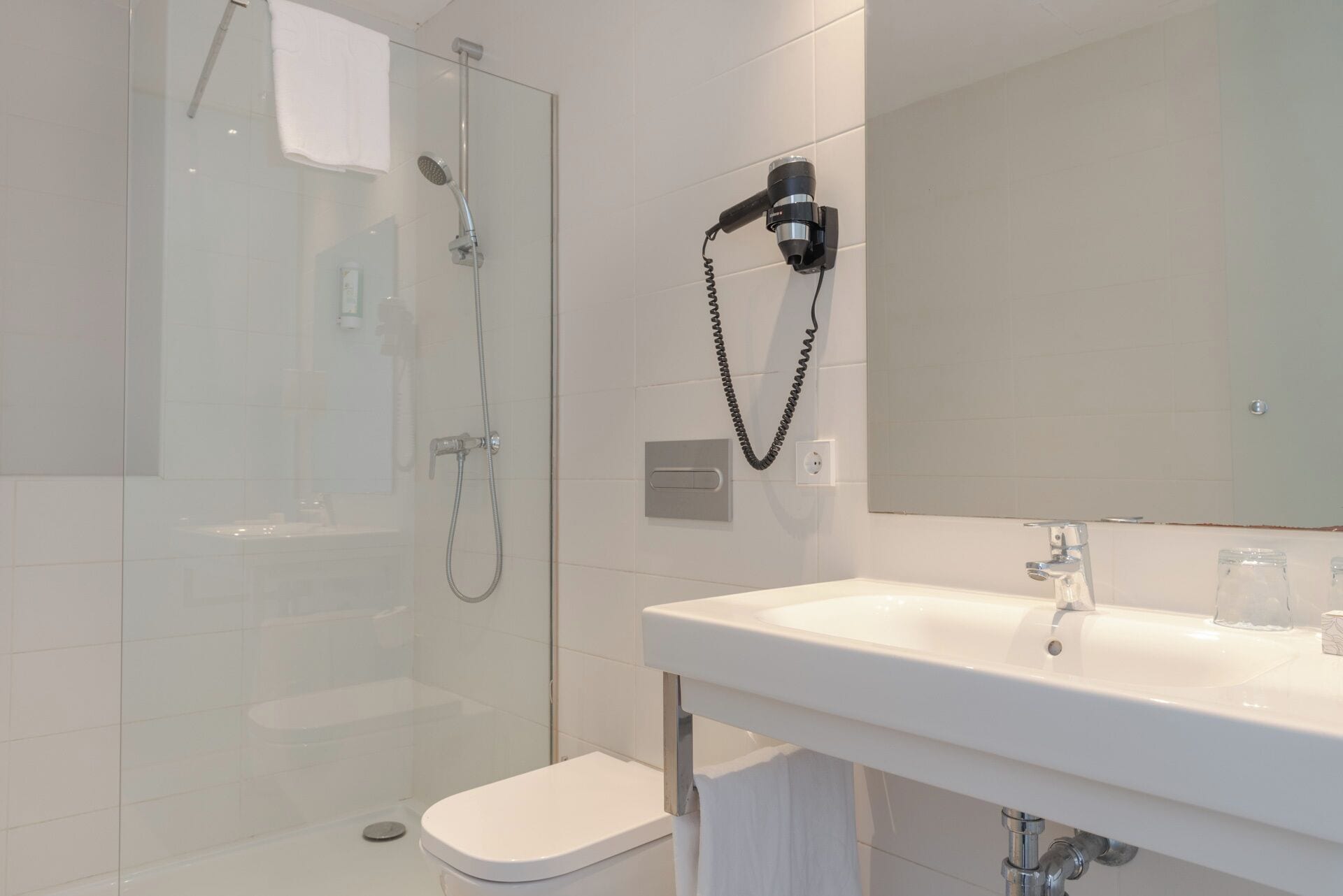 A modern bathroom with a glass-enclosed shower, a white sink, and a handheld hair dryer mounted on the wall.