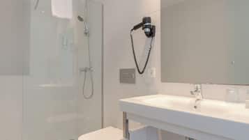 Ein modernes Badezimmer mit einer gläsernen Duschkabine, einem weißen Waschbecken und einem an der Wand montierten Haartrockner.