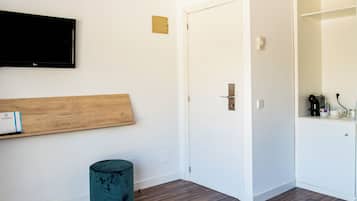 Une pièce avec une étagère en bois, un pouf turquoise, une porte blanche et un téléviseur à écran plat fixé au mur.