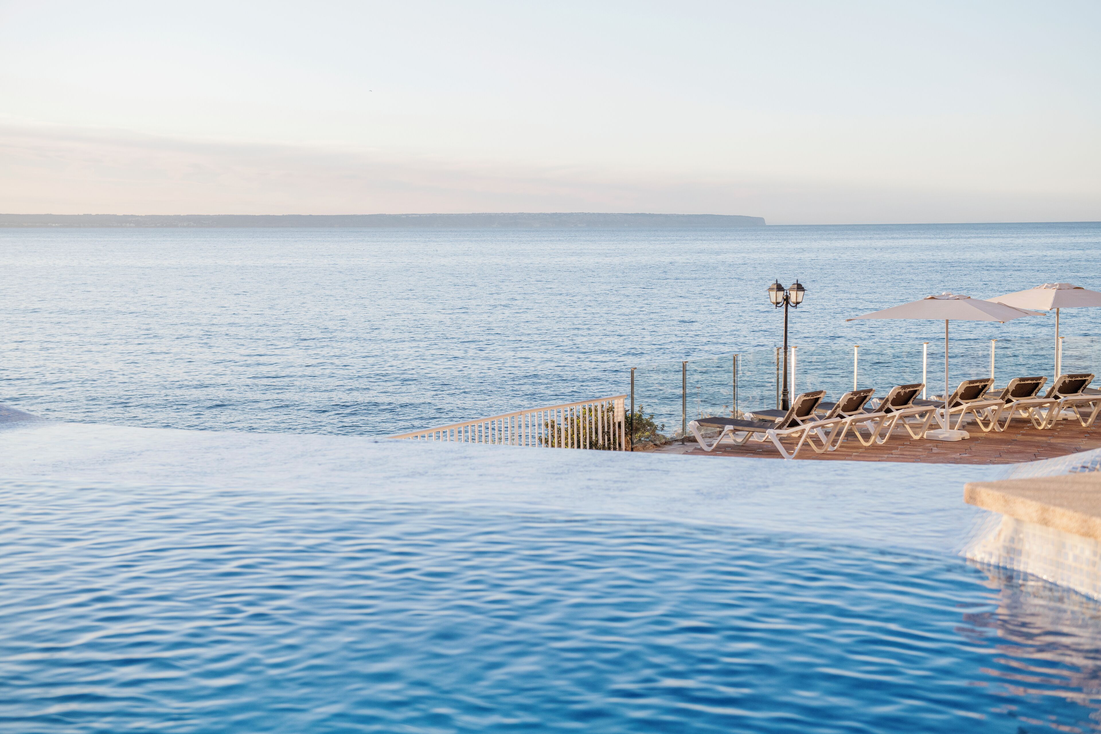 Zona de piscina con sillas reclinables y sombrillas, con vistas al mar tranquilo.