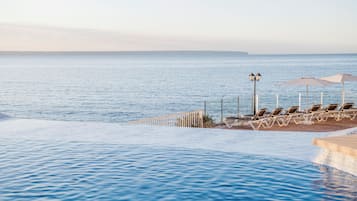 Zona de piscina con sillas reclinables y sombrillas, con vistas al mar tranquilo.