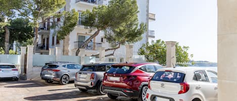 Un hotel con fachada blanca, varios balcones y coches aparcados delante.