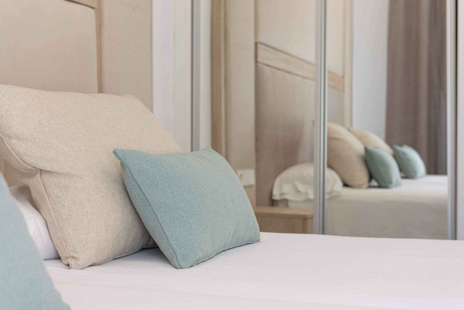A bed with two pillows, a mirror reflecting a bed with pillows, and a nightstand with a lamp.