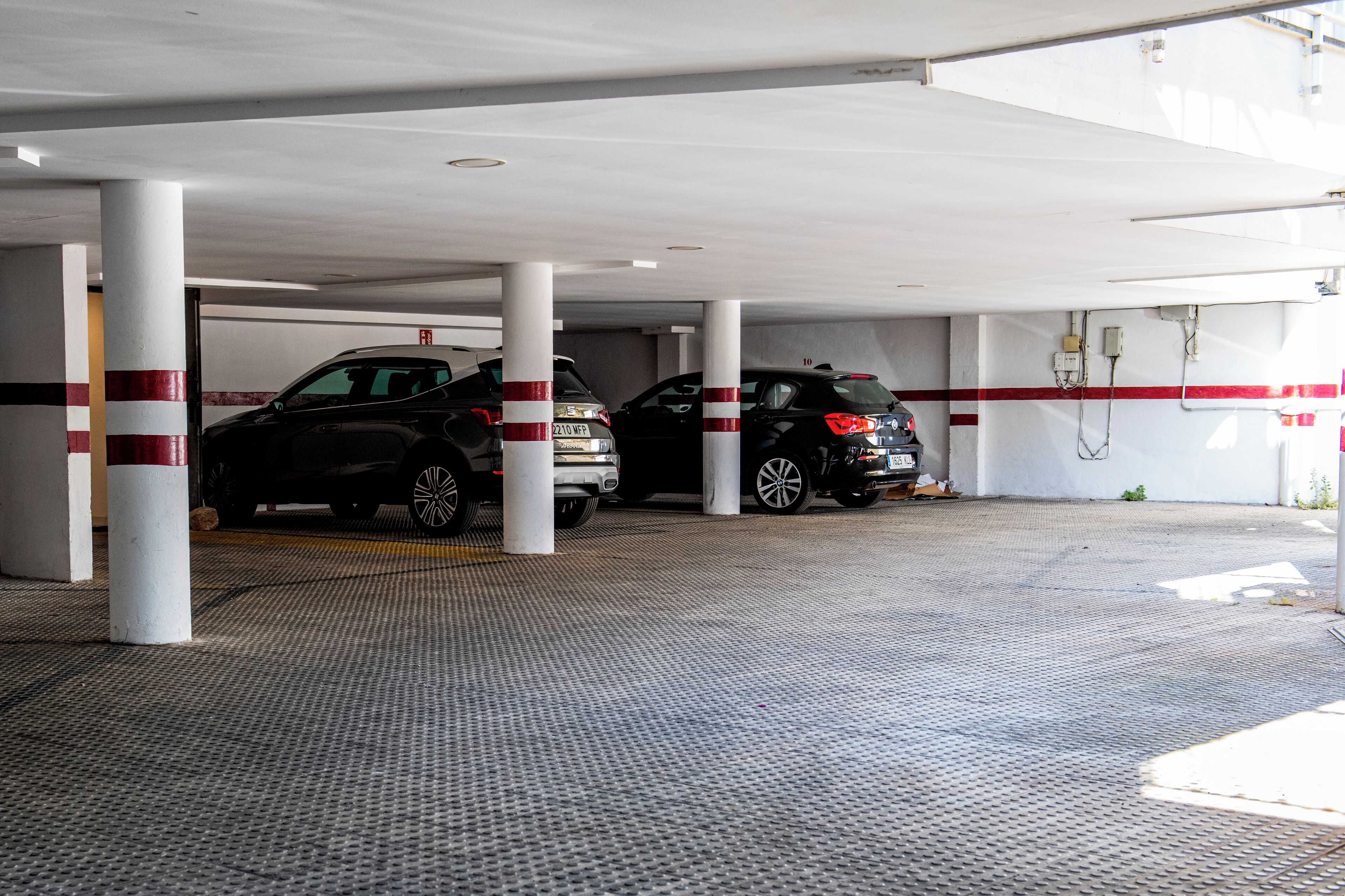 A covered parking area with two cars parked under white pillars with red stripes.