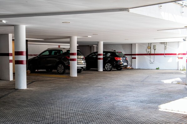 Katettu pysäköintialue, jossa on kaksi autoa parkissa valkoisten, punaraidallisten pylväiden alla.