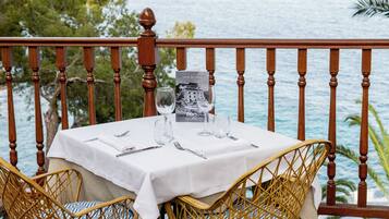 Mesa para dos con mantel blanco, dos copas de vino y una carta en un balcón con vista al mar.
