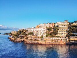 A coastal hotel with multiple floors, balconies, and a view of the sea.