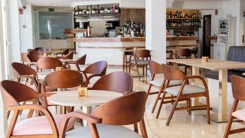 Un restaurant moderne avec des tables et des chaises en bois, un bar doté d’étagères remplies de bouteilles, et un intérieur propre et bien éclairé.