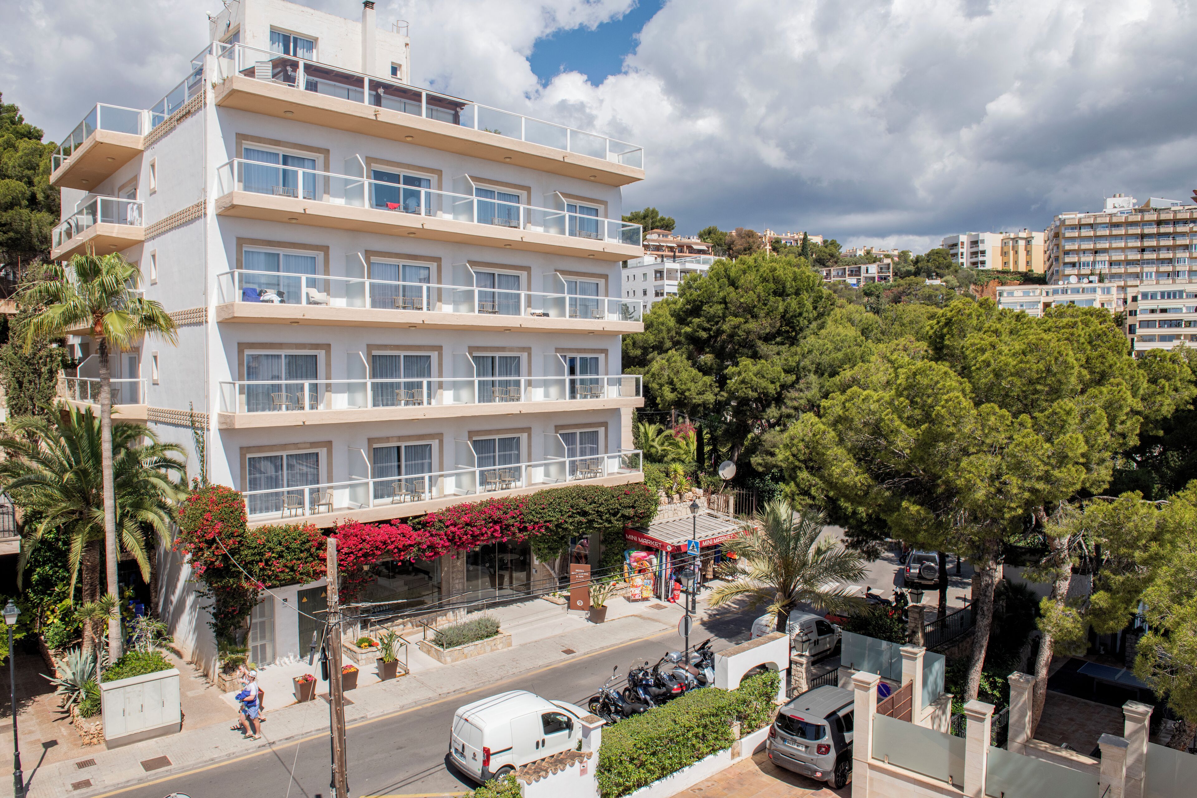 Un hôtel à plusieurs étages doté de balcons, d’un parking et d’une végétation luxuriante.