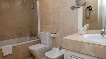 Un baño con bañera, inodoro, bidé y lavamanos con espejo.