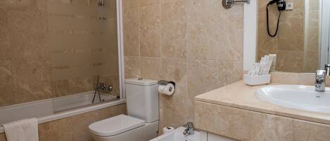 Un baño con bañera, inodoro, bidé y lavamanos con espejo.